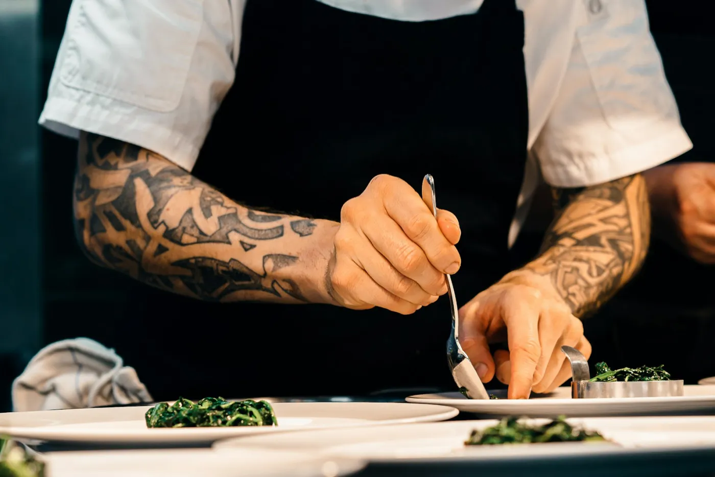 A chef's hands plating a dish at the pass