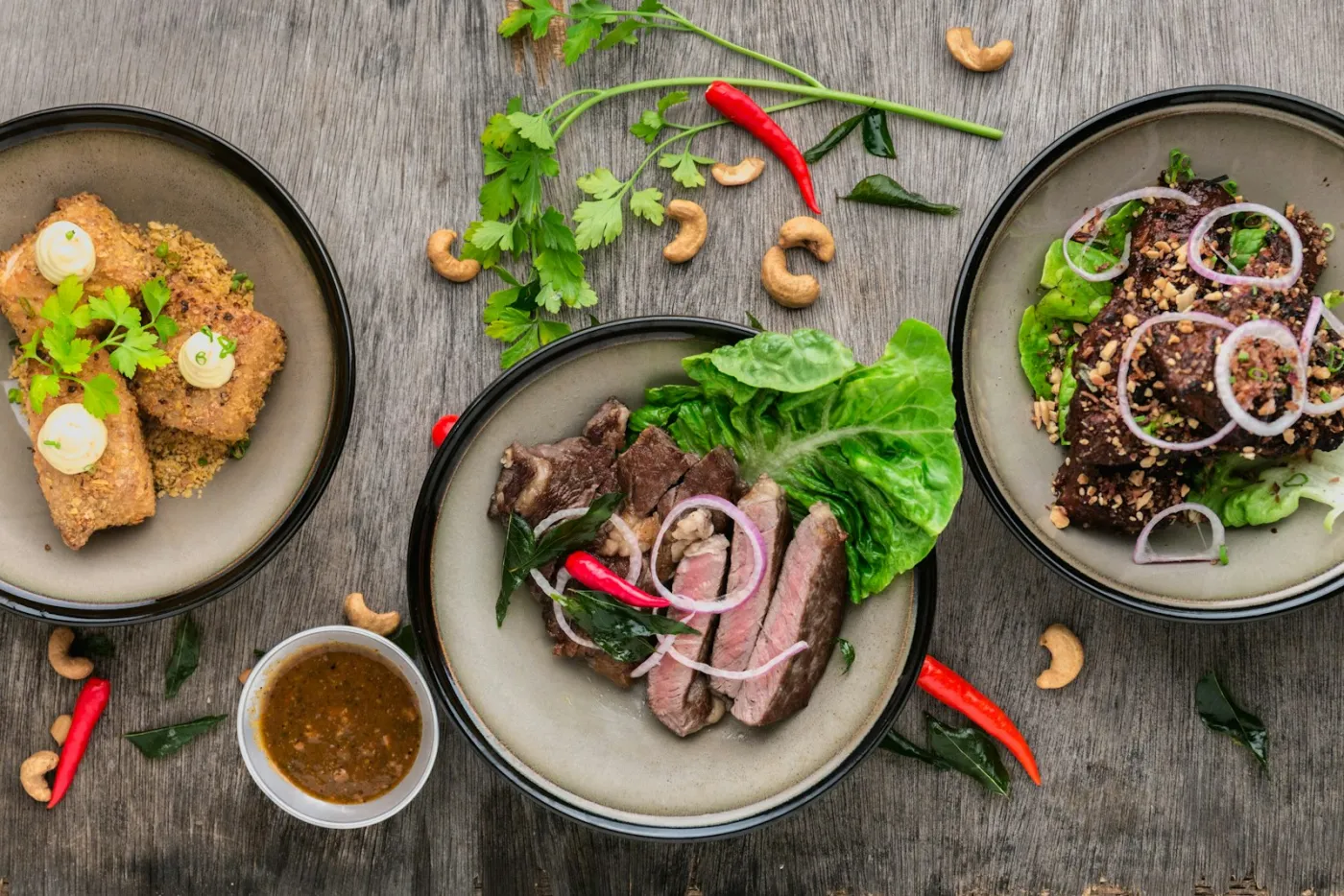 Plated dishes on a timber bench with fresh chillies, herbs and cashews